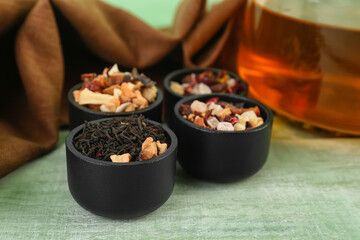 Bowls with different dried fruit tea on green wooden table, closeup