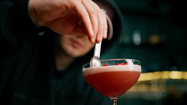 The bartender prepares a milk punch cocktail and puts chopped raspberries on top of the drink with tongs
