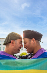Gay couple under LGBT rainbow flag while laughing and looking at each other. Concept of Pride....