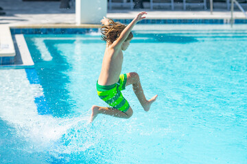 Kid jumping in water pool. Kid enjoying summer holiday, swiming in pool. Kid having fun on summer...