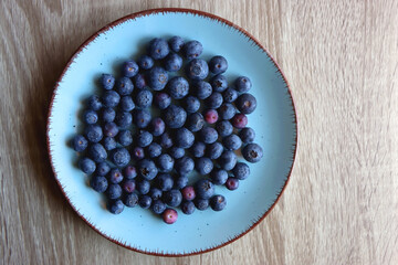 Turquoise plate with fresh blueberries on wooden background. Top view.