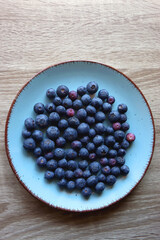 Turquoise plate with fresh blueberries on wooden background. Top view.
