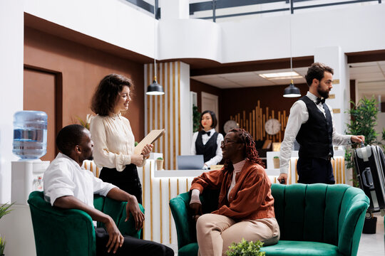 Woman welcoming hotel guests in lobby, providing excellent luxury service to people at resort. Young manager discussing about staff and accommodation with tourists, giving advice. Generative AI