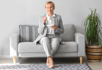 Mature businesswoman drinking coffee while sitting on sofa in office