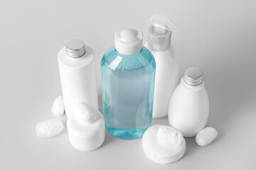 Micellar water with cosmetic products, cotton balls and pads on light background