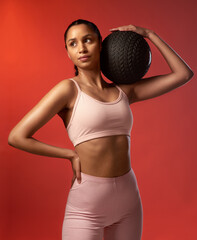 Focused and ready to smash another session. Studio shot of a sporty young woman holding an exercise ball against a red background.