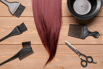 Red brown hair with brushes, bowl and scissors on wooden background