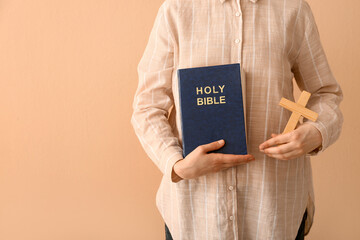 Fototapeta na wymiar Woman with Holy Bible and cross on beige background, closeup