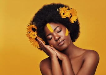 Her beauty is as delicate as a flower. Studio shot of a beautiful young woman posing topless with sunflowers in her hair against a mustard background.