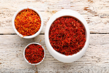 Bowls with pile of saffron on white wooden background