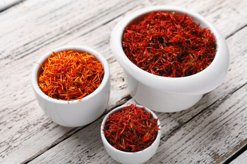 Bowls with pile of saffron on white wooden background