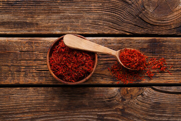 Bowl and spoon with pile of saffron on wooden background