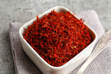 Bowl and spoon with pile of saffron on grey grunge background