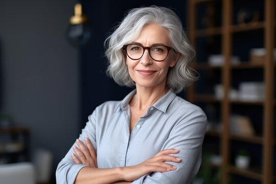 Smiling confident stylish mature middle aged woman standing at home office. Mature businesswoman, gray-haired lady executive business leader manager looking at camera arms crossed, generative AI