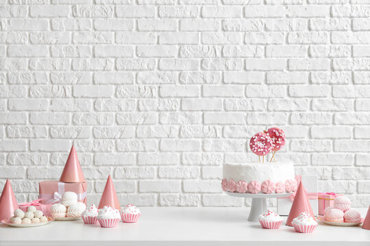Birthday cake with sweets on white table near brick wall