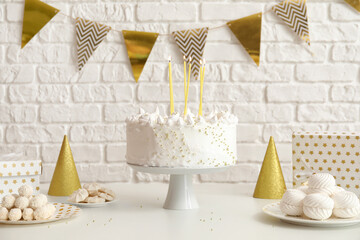 Birthday cake with candles and sweets on white table near brick wall