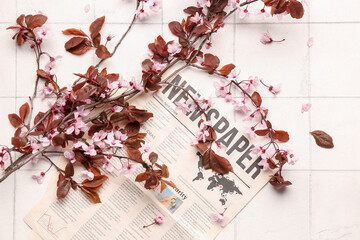 Beautiful blossoming branches and newspaper on white tile background