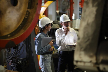  Supervisor Consults Young Engineer Working with big machine.