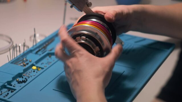 Male technician takes lens measurements with professional measuring tool, assembles cinema lenses for cameras in workshop on factory. Process of lenses manufacturing, assembly or Generative AI