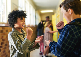 Im going to win this one. two young boys standing in the school hallway together and playing a game of rock, paper and scissors.