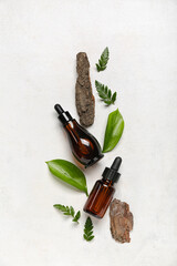 Bottle of cosmetic oil with plant leaves and tree bark on white grunge background