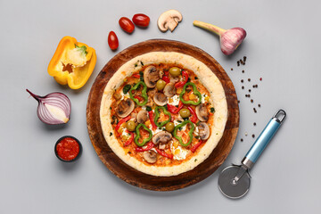 Board of vegetable pizza with ingredients and cutter on grey background