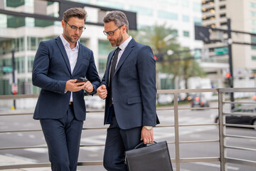 Business partners talking outdoor. Two businessmen discussing outdoor. Two business people talk project strategy. Two american businessmen in suits walk outdoors in the city and discuss business.