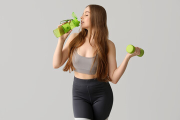 Sporty young woman with bottle of water and dumbbell on grey background