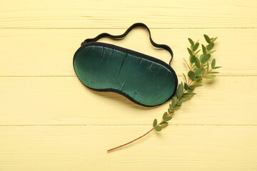 Sleeping mask and branch on yellow wooden background