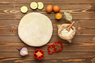 Raw dough and ingredients for preparing vegetable pie on wooden background