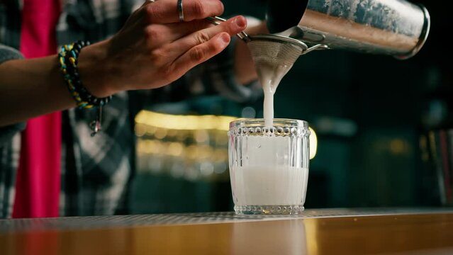 The bartender pours the finished cocktail into a transparent glass from a shaker through a strainer alcohol