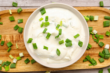Bowl of tasty sour cream with green onion on table, closeup