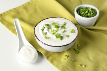 Bowl with sour cream and sliced green onion on white table