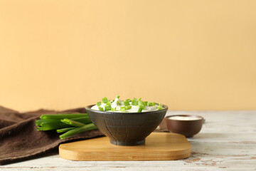 Bowl with sour cream and sliced green onion on wooden table near beige wall