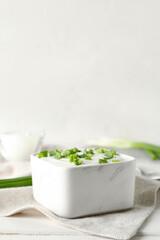 Square bowl with sour cream and sliced green onion on white wooden table near wall