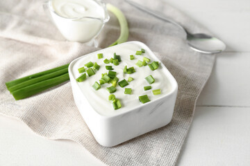 Square bowl with sour cream and sliced green onion on white wooden table