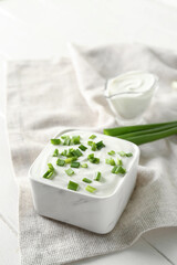 Square bowl with sour cream and sliced green onion on white wooden table