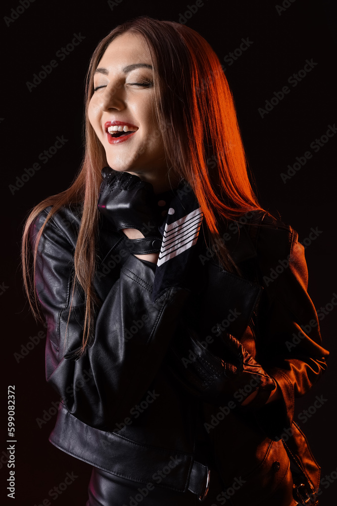 Poster beautiful young woman in leather gloves and jacket on dark background