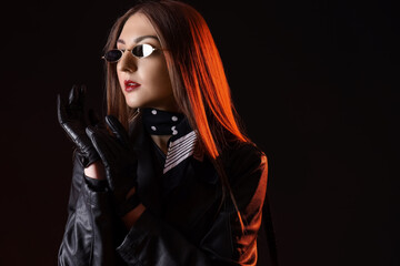 Beautiful young woman in leather gloves and jacket on dark background