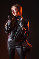 Beautiful young woman in leather gloves and jacket on dark background