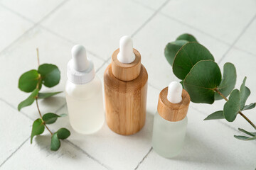 Bottles of cosmetic oil and eucalyptus branches on white tile