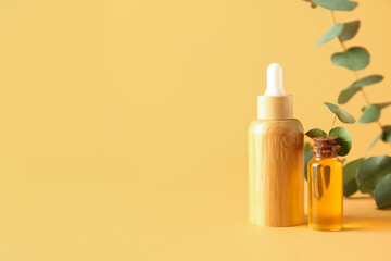 Bottles of cosmetic oil with eucalyptus branches on yellow background