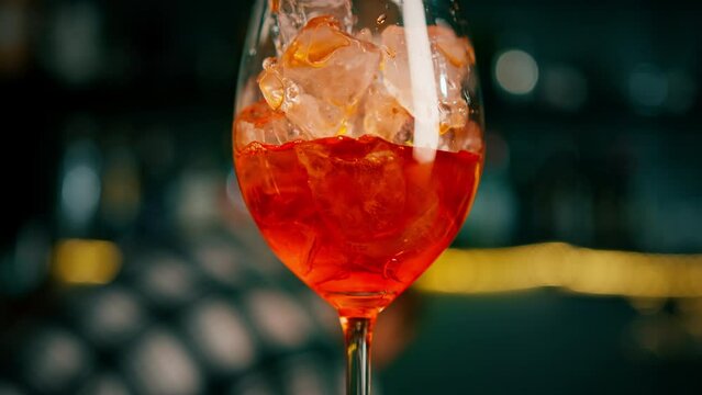 Preparation of Aperol Spritz cocktail bartender pouring prosecco into a glass with ice at the bar close-up