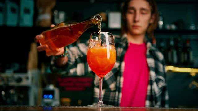 Preparation of Aperol Spritz cocktail bartender pouring prosecco into a glass with ice at the bar close-up