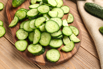 Board with pieces of fresh cucumber on wooden background