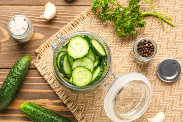 Jar with fresh cut cucumbers and spices on wooden background