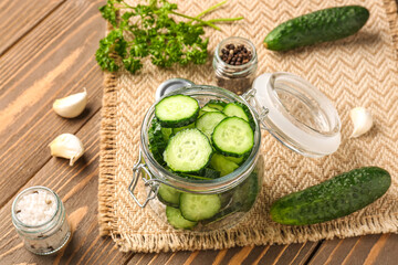 Jar with fresh cut cucumbers and spices on wooden background