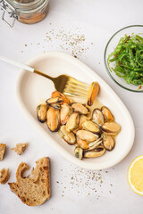 Plate with pickled mussels and bowl of seaweed salad on white background