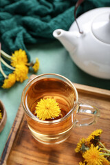 Board with glass cup of healthy dandelion tea and teapot on green background