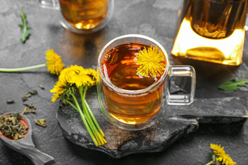 Board with glass cups of healthy dandelion tea on black background